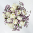 From an overhead angle, this bouquet appears as a tranquil, circular cluster of white and lavender, perfectly centred on a pure white background that enhances its serenity. Around a dozen white roses form the heart of the design, each bloom pristine and carefully positioned so the rose heads almost touch, creating a compact, harmonious ring. Some roses are still in bud, with petals wrapped closely together, while others are half-open or fully unfurled, revealing the soft spiral of their centres. Their colouring is a gentle, creamy white with delicate hints of ivory and buttery cream near the base of the petals, giving a sense of depth and natural warmth. Intertwined through the roses are generous sprays of Limonium in a cool lavender-purple, their many tiny blossoms forming a gauzy halo around and between the rose heads. This filler has a light, feathery quality from above, giving the impression of a fine, floral mist that softens the strong silhouettes of the roses and adds a quiet movement to the overall composition. Occasional glimpses of slender green stems and foliage give a reminder of freshly cut, living flowers rather than something overly stylised. Bathed in even, bright lighting, the bouquet looks almost like a comforting offering placed gently on a white altar. The feeling is one of peace, solace, and understated beauty, ideal for a condolence arrangement delivered to a home near Canonbury Station or a quiet gathering by Arlington Square, where simple, well-crafted flowers help convey sympathy, remembrance, and gentle support in times of loss.