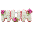 A thoughtfully arranged standing tribute spells out the letters MUM in bold, connected capitals against a clean white backdrop. Each letter is built from a dense carpet of pristine white chrysanthemums - their small, multi-petalled heads packed closely to produce a soft, cushion-like surface that reads as both pure and comforting. The edges of every letter are finished with a ruffled, light-pink ribbon trim that catches the eye and lends a gentle warmth to the otherwise serene white composition. Between the letters a subtle dark green support frame is visible, giving the piece a stable, upright presence suitable for a chapel, wake or graveside. To enliven the purity of the mums, three small posies of vivid fuchsia-pink roses are artfully nestled into the design: one at the upper left shoulder of the first M, another tucked into the curve at the base of the U, and a final cluster at the upper right of the second M. Each rose cluster includes glossy fern-like foliage and tiny coral-red hypericum berries that add texture and a faint, berry-like sweetness to the visual palette. The overall impression is tender and dignified, with the soft contrast between white blooms and pink accents suggesting both remembrance and affectionate celebration. In soft studio light the chrysanthemums read as luminous and calm, while the roses introduce a comforting splash of colour. As a local florist might explain to a bereaved family in Canonbury or nearby Islington, this MUM tribute conveys deep respect and love for a mother, combining classic sympathy blooms with refined craftsmanship and a quietly reassuring presence.