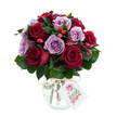 A sumptuous, hand-arranged bouquet of deep red and soft lavender roses sits against a crisp white backdrop, each bloom fully open with velvety petals unfurling in layers. The visual weight of the arrangement is rounded and dense, a close-knit chorus of crimson and burgundy roses balanced by lilac and dusty purple companions that lend a quiet, romantic coolness. Interspersed among the heads are bright red-orange rose hips that catch the eye with a glossy, tactile contrast to the satiny petals; their rustic, berry-like texture breaks up the roses' softness and brings an autumnal, hedgerow note to the bouquet. Dark green foliage - the smooth, lance-shaped leaves of ruscus or salal - forms a supportive collar, threading between blooms and giving the composition depth and shadow. The flowers are held in an antique-style mercury glass vase, its silvered, mottled surface shimmeringly reflective, bulbous at the base and narrowing toward the neck; a simple natural raffia tie around the neck adds an artisanal, country touch. A small rectangular white gift tag hangs forward from the twine, showing a tiny stylised rose illustration and room for a handwritten message. Soft studio light skims across the petals and the reflective vase, accentuating the saturated reds and the gentle mauves without creating harsh shadows. The overall impression is one of considered elegance - a bouquet that smells faintly of sweet rose and green leaf, designed to convey affection, celebration, or quiet sympathy. This arrangement feels right for an anniversary, a thoughtful thank-you, or to lift a living room with a touch of refined colour and texture; its classic palette and craftsmanship make it equally suitable for intimate moments and formal gifting.