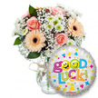 Against a crisp white background a cheerful 'good luck' gift ensemble is carefully composed: to the left and filling the midground, a generous bouquet sits in a clear glass vase, its neck casually tied with rustic twine that catches the soft studio light. The arrangement blends soft peach and powder-pink roses-petals tightly furled like satin-with warm peachy-orange Gerbera daisies whose dark brown centers give a quiet, earthy contrast. Wisps of white baby's breath (Gypsophila) thread through the blooms like delicate lace, while small clusters of white and lime-green chrysanthemum florets add a bright, almost citrusy note. Deep green foliage peeks from between stems, adding depth and a cool, leafy scent beneath the sweeter rose perfume. In the foreground to the right, slightly overlapping the lower edge of the vase, a round metallic silver foil balloon shimmers; its surface is scattered with tiny hearts, stars and playful confetti shapes in blue, pink, yellow and green. The balloon bears the jubilant message Good Luck! in a bubbly, multi-coloured font - the word Good punctuated by two yellow smiley-face 'o's, one winking and the other sticking its tongue out - and the word Luck! rolling in bright greens, oranges and blues with a final exclamation mark. The composition, lit evenly to emphasize colour and texture, reads as an encouraging, celebratory offering - ideal for send-offs, exams, interviews or new chapters - and feels like a thoughtful moment sent from a nearby Canonbury neighbour, ready for local delivery to Canonbury Square or Essex Road.