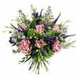 A lavish, hand-tied bouquet bursts into view against a simple white background, its rounded form packed with blossoms in gentle pinks, mauves, and purples that feel both romantic and modern. At its core, soft pink roses unfurl in layered spirals, some still shyly half-open and others fully spread, their petals transitioning from a deeper blush in the centre to quieter, almost creamy tones along the edges. Draped among them are generous carnations in dusty rose and muted mauve, their frilled petals forming plush, textured ruffles that invite the eye to linger. Cutting gracefully through this softness, tall spears of deep violet-blue Veronica add vertical structure and a touch of drama, a little like the upright silhouettes of trees lining Canonbury's calm streets. Rich purple lisianthus blooms and buds are nestled throughout, their velvety, bell-shaped flowers introducing a darker note of colour that grounds the palette. Threaded between the larger blooms are airy sprays of tiny, star-like aster flowers in soft lavender and periwinkle, giving the impression of a gentle floral haze. The whole arrangement is cradled in a bed of varied greenery: chartreuse, almost lime-green filler, delicate textured foliage, and cool, silvery eucalyptus leaves working together to frame and refresh the pink and purple tones. Below, the neatly aligned stems are visible, tied in a natural hand-tied cluster that looks ready to drop into a favourite vase on a Canonbury dining table or a studio near Highbury Corner. The bouquet radiates a feeling of affectionate celebration and quiet luxury, suited to birthdays, thank-you gifts, or a just-because delivery to brighten a home overlooking New River Walk.