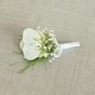 A single white orchid boutonniere rests on a softly textured, light beige fabric that looks like finely woven linen, the neutral background gently echoing the warm stone tones of Canonbury's quiet terraces. At the heart of the design sits a pristine Phalaenopsis orchid bloom, its broad, velvety petals opening in a graceful oval, creamy white with a subtle, sunlit hint of pale yellow and soft blush at the throat. The petals catch the light with a faint gloss, suggesting a fresh bloom just prepared by an experienced florist's hand. Encircling the orchid is a halo of delicate baby's breath, tiny Gypsophila blossoms forming a cloud-like ring of pure white that softens the outline of the boutonniere and adds an airy, romantic feel reminiscent of an intimate ceremony near Canonbury Station or along the leafy paths by Highbury Fields. Threaded between these miniature flowers are slender strands of feathery greenery, possibly maidenhair or a fine asparagus fern, their fresh green tones creating a quiet yet vibrant contrast against the white petals. The stems are neatly aligned and wrapped in a smooth white satin ribbon, the fabric pulled snug and finished with a small, tidy bow that hints at precise craftsmanship and care. The lighting is gentle and even, with no harsh shadows, so the textures of the ribbon, foliage, and orchid petals appear soft and touchable. Overall, the boutonniere feels calm, elegant, and timeless, the sort of refined floral accent a groom or groomsman might wear at a Canonbury townhouse wedding or a chic city celebration, carrying a whisper of fragrance and a sense of understated luxury on the lapel.