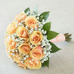 This arrangement reads like a delicate love letter in flowers: peach-hued roses gathered into a rounded cluster, their creamy-apricot petals layered so closely they almost invite a fingertip to trace their edges. Between and around those blooms floats a generous drift of white gypsophila, tiny star-like flowers that soften the silhouette and add a weightless, romantic air. Large, deep emerald leaves peek out beneath the blossoms, forming a lush, supportive frame that keeps the design feeling organic rather than overly structured. The stems are tightly wrapped with a textured blush ribbon finished with pearl accents, a small, elegant touch that gives the bouquet a personal, handcrafted feel. Photographed in gentle, diffuse daylight that flatters the pastel palette, the composition projects quiet anticipation - the sort of bouquet a bride might carry down a Canonbury lane or present during a vow renewal at a nearby church. The scent is clean and fresh: green, just-cut foliage mingles with the soft sweetness of roses and the faint, powdery note of gyp. As an Islington florist, Canonbury Flowers frames this bouquet for local celebrations and intimate ceremonies, and it travels well for morning deliveries around Upper Street, St Paul's Road, and Highbury Fields when requested by customers seeking understated romance.