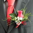This detailed image shows a handcrafted wedding boutonnière held gently in the palm of a skilled florist, as if mid-check before it is pinned to a suit for a Canonbury celebration. At the heart is a beautifully formed hot pink rose, its petals unfolding in tight, even spirals, with outer petals curving protectively around the centre like a quiet embrace. The shade is intense yet romantic, somewhere between fuchsia and raspberry, suggesting admiration and bright affection. Encircling the rosehead are airy sprays of white gypsophila, or baby's breath, their tiny, cloud-like blossoms providing a soft halo that lightens the composition, much like dappled sunshine in nearby New River Walk. Threaded through the arrangement, slender tufts of ornamental grass trace gentle arcs, adding texture and a sense of motion without disturbing the boutonnière's compact silhouette. A single deep-green leaf, its surface slightly waxy and reflective, forms a backdrop that gives structure and frames the rose with natural elegance. The stems at the base are bound in a narrow red ribbon, tied into a discreet bow that contributes just a hint of formality and flair, echoing the warm tones of a tie or pocket square. Behind the flowers, you can make out a dark, sharply tailored suit, the weave of the lapel lending a smooth, understated contrast to the softness of the florals. The atmosphere is one of calm anticipation and thoughtful detail, the kind of finishing touch chosen for a groom or special guest walking from a townhouse near Canonbury Place to a nearby wedding venue, carrying with them a small, fragrant symbol of love and commitment.