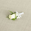 On a pale, finely woven fabric backdrop, a classic wedding boutonnière lies ready, its simplicity revealing the care of an experienced neighbourhood florist. At the centre is a single creamy ivory rosebud, just beginning to open, its petals smooth and gently spiralled like folded satin. Around it, clusters of delicate white baby's breath create a soft, misty collar, each star-like bloom adding texture without disturbing the calm elegance of the design. Fine strands of vivid green grass thread through the arrangement, some curling lightly around the rose, others extending outward in subtle arcs that give the piece movement and life, reminiscent of the greenery that lines Canonbury's quiet garden squares. The stems are tightly wrapped in gleaming white satin ribbon, the wrapping neat and even from top to bottom, ending in a refined bow that feels intentional rather than decorative. Light falls from above at a slight angle, catching the sheen of the ribbon and the faint gloss on the rose petals, while the textured background provides a soft contrast, like linen laid out in a calm bridal suite near Islington's side streets. The colour palette remains restrained - ivory, white, and fresh green - lending the boutonnière a serene, timeless quality suitable for grooms, best men, or cherished guests. Imagining it pinned carefully to a suit jacket, one can almost sense the cool touch of the rose, the feathery brush of gypsophila, and the gentle, understated fragrance that would accompany a wedding celebration in Canonbury.