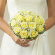 As a florist working in Canonbury, I often think of this bouquet as the neighbourhood's understated celebration: a compact dome of pale yellow roses, each one opened into a soft, layered rosette that reads as warmth and sincerity. The roses range from faint lemon to creamy butter, their velvety texture catching ambient light in a way that feels both luminous and intimate. Nestled between the larger blooms, delicate sprays of baby's breath float like tiny white constellations, lending an airborne softness that balances the roses' more substantial form. Around the perimeter, long, curved blades of dark green grass have been woven to create an architectural collar - a gentle frame that lifts and defines the shape without overpowering the florals. When held against bridal lace or a simple silk gown, the bouquet presents a calm, sophisticated silhouette and allows the bride's movement to remain the focus. There is a subtle fragrance here: a whisper of fresh-cut greenery blended with the faint honeyed note of the roses, powder-soft and comforting rather than heady. I imagine this arrangement arriving from our Canonbury Flowers workbench near Essex Road, carried along New North Road toward a small family ceremony by the Regents Canal - an emblem of devotion meant to be felt as much as seen. The overall effect is one of quiet optimism and refined simplicity: a keepsake of a wedding day that speaks of enduring tenderness and careful craftsmanship, chosen by someone who values grace and unobtrusive beauty.