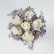 Soft elegance and timeless beauty define this overhead image of a compact bouquet, where six ivory-white roses gently spiral open at the core, each petal velvety smooth and untouched, gleaming under a diffused light. Lovingly arranged by the talented florists of Canonbury, these roses are ringed with a dreamy band of pale lavender filler, likely statice, which adds a feather-light texture and a muted haze of colour-a soothing counterpart to the crispness of the blooms. The fillers cluster densely, their tiny blossoms evoking the tranquil lilacs found in local Islington gardens, creating an embracing circle that frames the bouquet into a graceful, rounded whole. Placed on a pale, polished backdrop, the composition feels restful and refined, reminiscent of a quiet morning stroll near Canonbury Tower. The soft lighting flatters every curve, allowing the fresh whites and whispering purples to glow serenely. This arrangement radiates comfort and sophistication, making it perfect for bringing peace to a loved one, sending condolences, or simply adding a calming touch to a modern home near Canonbury Road. As the subtle fragrance drifts from the roses, this bouquet becomes a gentle, heartfelt offering-a true reflection of the elegant yet approachable spirit of Canonbury's community floristry.
