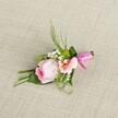 On a softly textured, pale linen background reminiscent of the calm interiors that grace Canonbury's elegant homes, a carefully handcrafted boutonniere awaits its moment. The central rose, a tightly furled bud in shades of blush and deep pink, exudes freshness and the promise of a romantic day. Flanking it, a light pink or peach alstroemeria unfurls its petals, revealing yellow accents and subtle markings-a delicate juxtaposition to the cloud-like white baby's breath and vivid green cushion mums that are carefully tucked among the layers. Fern-like sprigs arch gracefully upwards, adding a sense of airy movement, while broad, dark green leaves are folded artfully to create a supportive base. A dark green leaf wraps the stems, with a vivid fuchsia pink satin ribbon tied into a neat, gleaming bow at the base-a lively touch that catches the eye without overwhelming the arrangement's tranquil elegance. As daylight filters softly across the woven fabric, each detail-from the glossy ribbon to the intricate veining of petals-emerges with quiet vibrancy. Perfect for weddings or milestone celebrations throughout Canonbury and Islington, this boutonniere blends traditional beauty with modern artistry, and embodies the thoughtfulness and skill you might expect from a local Canonbury florist.