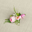 This boutonniere is captured as if paused between one cherished moment and the next, resting on a pale, gently woven fabric that could easily belong on a Canonbury dressing table before a wedding. At its centre, a cool pink rose rises slightly above the other elements, each petal shaped into a natural spiral that draws the eye inward. The petals hold a soft blush gradient, lightest at the edges and deepening toward the heart, like evening light gathering over nearby Islington terraces. Around the rose, pastel alstroemeria blooms open in slim, trumpet-like shapes, with creamy petals brushed with dusty pink and a soft glow of yellow at their cores. Fine lines and subtle speckles add delicate detail, giving the flowers a painterly quality. Tiny clusters of gypsophila - baby's breath - punctuate the composition with small white dots, airy and cloudlike, softening the outlines of the larger blossoms. Sprigs of slender greenery weave in and out, their cool green tones and feathery textures contrasting gently with the rose's velvety touch. All the stems are bound together by a neatly tied pink ribbon, glossy and carefully wrapped, creating a polished finish that suggests experienced, local hands at work. The light falls softly across the boutonniere, picking up the sheen of the ribbon and the gentle curves of the petals, emphasising the freshness of the flowers as if they've just arrived from an early-morning delivery to Canonbury Flowers. One can almost imagine the subtle fragrance: a hint of rose, a fresh green note from the foliage, something light and reassuring. Designed for special ceremonies - weddings, proms, intimate celebrations around Canonbury, Highbury, or Angel - this floral piece speaks quietly of affection, attention to detail, and the promise of a day to be remembered.