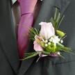 There is a quiet sophistication in this detailed buttonhole, captured on the lapel of a sharply dressed guest at a Canonbury celebration. The focus is on the interplay between the dusk-grey suit and the vibrant pop of a magenta pink tie, each element chosen to reflect the festive spirit found at local events from Douglas Road to Mildmay Park. The boutonniere itself glows in gentle light: at its centre, a delicate, pale pink rose unfurls serenely, its petals soft as silk. To its side, a partially open alstroemeria, marked with subtle purple-pink stripes, offers intricate contrast. Wisps of snowy gypsophila cluster around a single, emerald-green button mum, their textures forming a fresh, harmonious bed. Framing this, fine fern and slender greenery add a lightness reminiscent of a breezy Canonbury walk. The boutonniere is finished with a petite lavender satin ribbon, tied into a precise, glimmering bow that echoes the joyful hues of the tie. This arrangement, artfully constructed and perfectly placed, speaks of elegant local craftsmanship and love-filled occasions-a floral detail that brings an elevated charm to any joyous gathering in Canonbury.