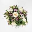 An overhead photograph shows a compact, hand-tied bouquet laid against a crisp, pure white background, so every blossom reads clearly, almost like a still life painted in soft light. At the heart of the design, creamy white and pale ivory roses spiral open in different stages of bloom - some tight buds with a hint of buttery yellow at their centres, others fully unfurled so you can almost feel the velvety texture of each petal. Threaded between them are elegant stems of alstroemeria, their long buds and half-opened blooms revealing petals washed in mauve, lavender and berry-pink, with faint greenish streaks that give the flowers a natural, painterly depth. Fine sprays of white gypsophila float between the larger stems like tiny clouds, softening every edge and filling the gaps with a delicate, airy lace. Deep green foliage forms a neat collar around the blooms, the broad, glossy leaves folding protectively to frame the arrangement and emphasise the freshness of each stem, as if it had just been conditioned in a Canonbury studio. The lighting is bright and even, evoking the feel of mid-morning daylight filtering into a townhouse off Essex Road, and allowing the subtle colour variations in the petals and leaves to stand out. The overall mood is one of calm elegance and gentle romance - the sort of bouquet you might send to a friend on New North Road to say thank you, or place on a small dining table near Canonbury Station for a quiet anniversary supper. Nothing in the image feels overcrowded or fussy; instead, the roses, alstroemeria and gypsophila work in easy harmony, creating a modern yet timeless floral piece that speaks softly of care, comfort and refined taste.