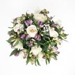 Top-down view of a circular hand-tied bouquet lying against a pure white background, the flowers appearing to float as if just set down on a studio table in Canonbury. At the centre, creamy white roses in shades of ivory and pale champagne open in full spirals, some tightly cupped, others more relaxed, each petal curling softly like folded silk. Threaded between them are slender buds of purple alstroemeria, their outer petals a deep lavender and rich plum that melt into fresh green at the tips, suggesting blooms on the verge of opening. Tiny white baby's breath is scattered throughout, forming a fine, cloud-like veil that lightens the arrangement and adds a sense of breath and space between the larger flowers. Around the outer edge, broad, glossy dark green leaves create a natural collar, framing the bouquet and giving it depth and structure, much like the greenery you'd see along the tree-lined streets near Canonbury Square. The lighting is gentle and even, with no harsh shadows, so every texture is visible-from the velvety rose petals to the slightly waxy alstroemeria buds and the feathery gypsophila. The overall impression is calm, refined elegance with a quiet hint of romance, suitable for a thoughtful anniversary surprise, a wedding detail, or a comforting gesture of sympathy delivered to a home off Essex Road. Though the image is still, the mix of open and budding blooms suggests ongoing life and hope, like a moment of stillness in the middle of a busy North London day.