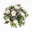 Viewed from directly above, this sympathy bouquet appears as a soft, rounded cushion of flowers and foliage resting on an immaculate white background, like a quiet moment suspended in time. At its centre, the eye is drawn to a cluster of creamy white roses, their petals smooth and velvety, unfolding in graceful spirals that move from pure white edges into a faint ivory and blush-peach glow at the heart. Some of these roses are fully open, revealing every delicate layer, while others are still partially closed, their gently cupped forms suggesting tenderness and restraint. Woven among them, slim stems of purple alstroemeria buds introduce subtle colour, with tips washed in lavender and deeper violet, fading into fresh green and pinkish tones as they approach the stem. Many buds remain sealed tight, promising blooms yet to appear, while a few offer tiny glimpses of the striped inner petals, adding a sense of quiet anticipation. Scattered throughout, sprigs of white baby's breath bring a gossamer lightness, each tiny blossom like a floating dot of softness, giving the arrangement an almost cloud-like aura. Encircling everything, rich, dark green leaves form a lush base, their surfaces slightly glossy, catching gentle highlights that accentuate the bouquet's rounded shape. The overall effect is peaceful and composed, the kind of arrangement a Canonbury family might choose for a thoughtful delivery to a loved one's home off Essex Road or to rest beside a candle at a small memorial. It radiates calm support, understated beauty, and a sense of comfort that lingers quietly in the background.