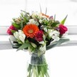 A joyful, contemporary bouquet bursting with colour and texture, as if freshly gathered from the private gardens that dot the streets of Canonbury. At its glowing heart, a radiant orange Gerbera daisy unfurls with effortless charm, surrounded by a symphony of roses in magenta, fuchsia, and deep red-a celebration of romance and spirited elegance. Creamy white alstroemeria with their distinctive speckled markings stretch outward, creating a sense of abundance and light, while clusters of petite, daisy-like white chrysanthemums add a frothy, playful finish. Here and there, soft touches of pale yellow roses and sprigs of lavender hint at the seasonal variation and quiet diversity found throughout Islington's winding lanes. The whole arrangement is enveloped in glossy broad-leaf greens and slender, arching foliage, adding drama and luxurious dimension, all resting in a clear glass vase that glistens in the soft daylight. The visible stems, immersed in pristine water, serve as a reminder of the flowers' unrivalled freshness and the skill of Canonbury's local florists. Designed to brighten celebrations-whether birthdays by the New River Walk or spontaneous congratulations near Canonbury Square-this bouquet captures the uplifting, modern spirit of the area and delivers a heartfelt message of happiness, renewal, and sincere affection.