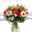 This vibrant floral composition is a joyful medley of colour and texture, crafted to animate any room or moment in Canonbury's lively heart. Pizza-slice orange gerberas and gentle peach blooms radiate warmth like the first rays over Highbury Fields. Vivid magenta roses, with their plush, spiralling petals, evoke romance and a touch of classic London grandeur. Sprigs of ivory alstroemeria and petite white blossoms peek through dense greenery, lending the bouquet both brightness and a hint of delicate fragrance that stirs memories of local gardens on a fresh morning. Framing the bouquet, broad, glossy aspidistra leaves curve gracefully, offering both structure and a sense of embracing comfort, much like the welcoming parks of Canonbury itself. Set in a clear glass vase, every leaf and stem is showcased, imbuing the entire piece with an unmistakably fresh, hand-tied quality. This arrangement feels ideal for celebrating milestones, expressing heartfelt thanks, or simply uplifting a loved one's day-infused, as always, with the warmth and authentic artistry that define the neighbourhood's favourite florists.