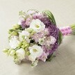 A gracefully arranged hand-tied bouquet, expertly crafted near the heart of Canonbury, radiates a soft palette of white, blush pink, and lilac. Anchored by lush white lisianthus-each flower with layered, silken petals cradling a yellow center-and framed by an ensemble of unopened buds, the bouquet captures local freshness and early spring promise. Ruffled clusters of pink and lavender stock intermingle, their delicate blooms woven through the composition, highlighted by the striking presence of deep violet Allium 'Star of Persia'. The alliums' spiky globes provide captivating contrast, rising above the harmonious pastels with modern flair. Wisps of slender green foliage arc delicately around the bouquet, echoing the verdant embankments of New River Walk. Every detail, from the rounded, softly elongated silhouette to the skillful spiral of fuchsia pink satin ribbon and gleaming white pearls binding the stems, reflects the artistry of Canonbury's florists. As natural light falls gently across the bouquet, subtle textures and colour nuances come alive, conjuring a mood of romance and refined celebration. Perfect as a bespoke bridal bouquet for local weddings or an elegant table centerpiece for gatherings on Canonbury Park North, this arrangement embodies the trending pastel palette and sophisticated yet inviting style adored throughout the neighbourhood.