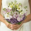There's a poetic tranquility to this Canonbury wedding bouquet, captured just as it's cradled in the bride's hands, her soft pink nails a gentle echo of the pale pastels within. Creamy white Lisianthus unfurl their ruffled petals, paired with unopened buds that hint at a fresh start amid the spring air by the New River Path. Feather-light stocks in blush pink and lilac cluster around the Lisianthus, building layers of cloudlike texture as sweetly scented notes evoke memories of local blossom-filled gardens. At the base, a striking band of spiky, star-shaped purple Allium offers both architectural curiosity and modern beauty, grounding the arrangement with its vibrant color and sculptural form. Artful loops of glossy green bear grass tie the composition together, lending both structure and a nod to the winding green lanes of Canonbury. The bride's ivory dress, glimpsed blurred in the background, harmonizes with the bouquet's palette while ensuring the flowers remain the undisputed focus. Brought together with a careful yet effortless grace familiar to the artisans of Canonbury Flowers, this bouquet feels as if it has gathered all the hope, romance, and springtime renewal of the area into one harmonious display-ideal for a joyful, heartfelt celebration.
