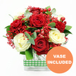In this photograph, a richly textured bouquet of red and white roses sits proudly against a bright white background, evoking the feeling of a special occasion unfolding in a Canonbury home. Deep, velvety red roses open fully, their petals layered in generous spirals, while creamy white roses nestle among them, offering a softer, more luminous note that enhances the romantic contrast. Threaded between the roses are delicate sprays of tiny red filler flowers, similar to dyed gypsophila, their fine stems and miniature blooms adding a feathery, cloud-like softness to the design. Round red hypericum berries, smooth and polished, are dotted throughout the arrangement, catching the light like small, festive baubles and contributing a joyful, celebratory spirit. Lush greenery, including cool-toned eucalyptus and mixed leaves, spills gently around the blooms, framing the central roses and adding depth, texture, and a sense of natural movement, as if freshly gathered from a walk near Highbury & Islington. The flowers are arranged in a modern clear glass rectangular vase, its transparent sides revealing the neatly aligned stems and lending a sleek, urban look that pairs well with Canonbury's mix of period and contemporary interiors. A green and white gingham ribbon wraps around the vase's centre, offering a charming, rustic accent reminiscent of a relaxed brunch or evening gathering on a local garden terrace. In the bottom right corner of the image, an orange circular emblem with crisp white lettering states VASE INCLUDED, indicating that this tender, romantic rose arrangement arrives ready to display, perfect for anniversaries, Valentine's gestures, or simply bringing warmth and colour into a North London living space.