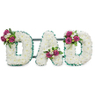 A carefully composed memorial piece spells the word DAD in large, capital letters, each letter built up from a dense carpet of pristine white chrysanthemums (or similar cushiony white florets) that read as soft, cloud-like surfaces. The blooms are closely packed so the letters appear almost sculpted, their gentle curves and bold strokes catching soft, diffused light as if lit by a calm morning over Canonbury Square. Each letter is crisply outlined with an emerald green, pleated or ruffled ribbon that traces both the outer and inner edges, the cool green rim giving the white a clear, dignified edge and a subtle sense of formality. Behind the word a narrow, dark green or grey horizontal support bar sits discreetly, suggesting the piece is designed to stand securely at a service or graveside. Accent clusters of deep magenta-pink roses break up the white expanse: a compact spray on the upper left curve of the first D, a graceful nest of blooms tucked into the lower central V of the A, and a mirrored cluster on the upper right curve of the second D. Small white freesia or similar tiny white blossoms peek among the roses, adding delicate scent and a fine-textured contrast to the round chrysanthemum heads, while rich dark green foliage gives the composition depth and a natural frame. The overall effect is one of respectful warmth-a personalized, handcrafted tribute that reads as both a clean, formal statement and a quiet, loving farewell for a father-suitable for funeral displays near Upper Street or local Canonbury memorial services.