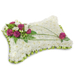 A rectangular pillow-shaped funeral tribute sits against a clean white backdrop, its shadow soft and unobtrusive, created to read as a quiet, comforting presence. The entire cushion is densely carpeted with hundreds of small, pure white chrysanthemum florets; their tight, layered petals form a cloudlike, plush surface that invites a gentle touch and suggests calm and purity. Along the lower edge a neat scalloped trim of folded lime-green satin ribbon frames the piece, the cool sheen of the fabric creating a subtle ruffle that both defines and freshens the silhouette. In the upper left corner a concentrated cluster of deep fuchsia roses gathers like a warm memory-velvety petals unfurling rich colour-interspersed with delicate white freesia or lisianthus that lift the composition with a whisper of fragrance and delicate form. Lush green accents-feathery fern fronds and glossy leaves-surround and support the cluster, adding depth and a living contrast to the white chrysanthemum field. Three slender, dark green bear-grass blades arch gracefully across the white surface, their elegant curves drawing the eye diagonally and giving motion to an otherwise serene scene. Mirroring the main spray, a single fuchsia rose nestles near the opposite corner, balanced among small green leaves and completing the visual conversation. The lighting is soft and even, catching the satin ribbon and the velour of the roses while preserving the chrysanthemums' matte softness. This pillow is deliberately composed to symbolise peaceful rest and reverent remembrance-the tactile textures, gentle scent, and considered balance make it a thoughtful sympathetic tribute suitable for memorial services in Canonbury and neighbouring Islington.