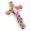 This image shows a beautifully abundant floral cross, captured on a pure white backdrop that allows every flower to stand out in clear detail. The cross is slightly angled, with the top leaning toward the viewer's left, giving a sense of depth, as though it has just been set down by a careful pair of hands in a Canonbury church or family home. Along its outer edges runs a thick, snowy band of white spray chrysanthemums, tightly packed so no gaps show, creating a clean, sculpted silhouette that feels soft and comforting. Peeping from behind this cushion of white, a continuous strip of light green ribbon or wrapped foliage forms a slim border, adding a gentle, fresh outline around the entire tribute. Inside the cross, the flowers are densely arranged, with no visible foliage, forming a lush, continuous surface of colour. Large roses in vivid fuchsia pink and gentle creamy yellow are spaced artfully along the arms and down the length, their open blooms offering a sense of generosity and love. Nestled between these roses are clusters of bright lime-green button chrysanthemums, their rounded forms and intricate petals adding lively texture without disturbing the solemn mood. Threaded among them are smaller, deep purple and violet flowers, such as lisianthus or statice, their rich hues adding depth and a quiet, reflective tone, like the shaded paths around Canonbury's green spaces. The bright, even lighting shows every fold of ribbon and every petal clearly, making this floral cross a fitting Christian sympathy piece for funerals, memorials, or graveside tributes, expressing both grief and a gentle celebration of life.