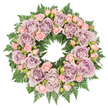 A serene, circular funeral wreath is displayed from a bird's-eye view against a bright white background, its quiet elegance immediately evoking remembrance and peace. The ring is densely packed with flowers, the most striking of which are large, fully opened roses in muted shades of lavender, dusty mauve, and greyish violet. Their layered petals create a soft, velvety texture, curling gently inward and outward like the pages of a cherished story. Threaded thoughtfully among these larger blooms are sprays of smaller blush pink roses, some still in bud, others half-open, lending a sense of unfolding tenderness that balances the more sombre purple tones. The colour palette feels calm and sophisticated, perfect for paying respects at a church service near Canonbury Square or a farewell held in a local crematorium chapel. Every flower sits upon a thick foundation of deep green fern fronds, whose feathery, serrated leaves form a lush halo of foliage around the ring. The ferns extend slightly beyond the roses, framing them with natural structure and adding a comforting woodland feel, like the soft greenery you might see in nearby Highbury Fields after rain. Glimpses of darker filler greenery and tiny buds tucked between the blooms add subtle shadow and depth, keeping the arrangement from feeling flat despite its overhead presentation. The lighting is gentle and even, allowing the pastel and jewel-like tones to harmonise without glare. This wreath reads as a thoughtful, lovingly arranged tribute, crafted by a florist who understands how flowers can offer quiet support and dignity in times of loss across the Canonbury community.