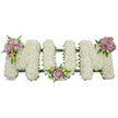 A tender funeral tribute formed in bold capital letters spelling MUM, each letter built from thousands of small, snowy-white chrysanthemums packed densely to create a cloud-like, softly textured surface. The trio of letters stands three-dimensionally against a bright white background, the pristine blooms speaking of purity and peaceful remembrance. Soft clusters of lavender and pale pink roses are placed as gentle punctuation: one cluster rests on the upper left arm of the first M, another nestles in the graceful curve of the U, and a third highlights the upper right arm of the final M. These pastel roses - some fully open, some in tight bud - add velvety scent and a warm, personal note amid the crisp white. A wash of rich green foliage, including slender fern fronds and lighter, fresh green leaves, frames each cluster and slips between the chrysanthemums, giving depth and a cool colour contrast. Along the base and faintly visible beneath the blooms, a dark green structural frame - ribbon-wrapped or moss-covered - provides subtle support, its outline anchoring the letters. Soft, diffused lighting suggests an indoor funeral setting, where the arrangement reads as a calm, reverent presence. The overall effect is one of careful craftsmanship and quiet consolation: a classic sympathy tribute appropriate for a mother's service, wake, or graveside, intended to honour memory with dignity and gentle beauty. For families in Canonbury and nearby Islington, this design conveys love, respect, and a peaceful farewell in both sight and scent.