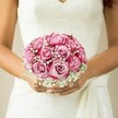 Cradling this exquisite bouquet against her lace wedding dress, a Canonbury bride stands wrapped in the anticipation and promise of her big day. The bouquet is a celebration of romance and local artistry: roses that glow with a gradient from gentle blush to vibrant magenta, each petal soft and fresh beneath the subtle shimmer of morning light filtering through Islington's leafy streets. Wisps of tiny white baby's breath encircle the roses, lending a gentle, mist-like texture that tempers the blooms' exuberant colours and offers a serene counterbalance. Resting in warm, lightly tanned hands with delicately manicured nails, the bouquet radiates harmony-the compact, rounded shape whispering of tradition while the textural interplay hints at bespoke modern style. The dress's intricately patterned lace bodice and flowing sash add a tactile, painterly layer that ties everything together. A neutral, softly blurred backdrop envelops the scene, sharpening the emotional gravity at its core: the joyous hope, love, and artistry that define weddings in Canonbury. For a bride seeking both classical beauty and a touch of neighbourhood elegance, this bouquet tells a story as vivid as any memory.