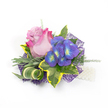 Against a clean white backdrop, this compact corsage reads like a little portrait of summer evenings in Canonbury: a single elegant rose takes centre stage, its petals graduating from a soft lavender-pink at the heart to a vivid fuchsia at the outer edges, the velvety folds catching a gentle, natural light. To the right, a cluster of indigo-purple florets-suggestive of hydrangea or periwinkle-brings a jewel-like contrast, each tiny blossom marked by bright blue and lime-yellow centres that twinkle like sunlit dewdrops. The blooms are cradled by a studied chorus of foliage: broad, variegated ivy leaves with deep emerald centres and warm golden-yellow margins give solidity and a classic silhouette; slender, silvery-green leaves-reminiscent of lavender foliage-soften the palette with muted texture; and a sculptural striped leaf of green and cream curls gracefully, lending a contemporary twist.
Delicate, airy sprigs of lighter green-similar to asparagus fern-thread through the composition, adding a sense of motion and breath. Beneath, an intricate web-like layer of dark purple mesh peeks out, its open weave creating depth and a subtle, modern shimmer. On the lower right, a short strand of lustrous white pearls suggests the attachment or wristlet, catching highlights against the white ground. The overall impression is romantic yet modern: tactile, fragrant, and meticulously balanced-ideal for weddings, prom or milestone celebrations. The corsage's restrained palette and thoughtful textures invite both sight and touch, offering the quiet pleasure of a handcrafted floral accessory ready to accompany someone along Canonbury's leafy lanes or to a celebration at nearby Canonbury Square.