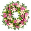 A sumptuous circular memorial wreath in harmonious shades of pink, cream, and fresh green stands out vividly against a clean white background, its shape symbolising an unbroken circle of love and remembrance. The wreath is thickly adorned with roses in deep magenta, rich fuchsia, and soft blush pink, their velvety petals layered from tight buds to wide-open blooms that seem to cradle the centre of the design. Between these roses, large double lilies add an elegant, almost sculptural presence, with petals in creamy white, pale pink, and delicate peach tones, some fully unfurled and others held in smooth, lime-green buds that lean gently outwards. A generous base of greenery supports and frames the flowers, featuring dark emerald foliage, feathery fern fronds with intricate, lacy leaflets, and broader glossy leaves that add both depth and contrast. The abundance of foliage creates a natural, garden-like feel, as if the wreath had been gathered from a well-tended Canonbury garden near New River Walk on a calm morning. The stark white backdrop isolates every detail, making the interplay of colours and textures easy to imagine: the cool touch of the leaves, the softness of the petals, and the quiet, respectful mood they create together. This wreath is perfectly suited for funerals, remembrance services, and celebrations of life held in local Canonbury churches or crematoria, offering a dignified, comforting floral tribute that reflects both the beauty of the area and the care of the florist who crafted it.