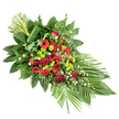 An elegant funeral spray is shown against a stark white background, its form flowing from a structured upper corner into a softer, tapered tip, like a gentle arc of colour and foliage. The central area is richly packed with deep red blooms: velvety roses from tight buds to fully opened flowers, bold red gerbera daisies with shadowy centres, and softly frilled carnations that add volume and texture. Interspersed among these are vivid lime green chrysanthemum pompons, whose rounded, almost button-like heads introduce a bright counterpoint and a more contemporary feel. Tiny white filler flowers, similar to miniature daisies or gypsophila, are dotted through the arrangement, bringing subtle lightness so the overall design feels soothing rather than heavy. This lush bed of blooms is supported by generous layers of greenery. Broad, glossy dark green leaves hug the flowers closely, while finer, feathery ferns and other textured greens extend beyond, shaping the long, elegant silhouette of the spray. On the lower right, several long, blade-like leaves fan outward, enhancing the sense of movement along the length of the design, reminiscent of a spray that might be placed along a casket at a Canonbury church or in a quiet chapel near Upper Street. At the upper left, a structured bundle of straight stems or leaves rises upwards, with one wide leaf wrapped neatly around its base, giving the piece a polished, contemporary accent. The finished tribute feels both vibrant and composed, suited to a memorial or funeral service where families wish to honour a loved one with a striking yet respectful floral display.