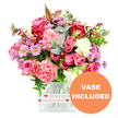 A lavish, hand-crafted bouquet pours from a clear, square glass vase, photographed against a pure white background that throws every bloom into sharp relief. At the heart of the arrangement are plush pink roses, some opening wide in rich fuchsia and magenta tones, others softer and more demure in pale blush and pastel pink, giving the bouquet a layered, romantic personality. Between them, ruffled carnations in coral, peach-pink, and light salmon shades create a sense of softness and movement, their petal edges delicately frayed. Tucked among the larger flowers are clusters of daisy-like chrysanthemums in lavender and soft purple, their bright green, button-like centres adding a lively spark, alongside a scattering of creamy white blooms that gently calm the richer colours. Surrounding and weaving through the flowers is an abundance of greenery: rounded eucalyptus leaves with a cool, silvery-green tint, darker green foliage that deepens the composition, and a few reddish-brown accents that suggest an intimate, romantic warmth. The vase has a sleek, modern squared form, its base wrapped in a white band decorated with repeating red hearts and the phrase all my love written in flowing red script, clearly echoing the sentiment behind the gift. In the lower right corner of the photograph, an orange circular badge with bold white capital letters reads VASE INCLUDED, signalling that this is a complete, ready-to-display floral present. The bouquet feels like something created in a Canonbury flower shop for same-day delivery around St Paul's Road, Aberdeen Park, or nearby tree-lined terraces, ideal for Valentine's Day, Mother's Day, anniversaries, or any moment when you want to send a burst of colour, fragrance, and heartfelt affection.