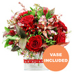 A richly romantic bouquet brimming with red tones is pictured against a clear white background, echoing the poised elegance of a freshly finished design at a Canonbury Flowers worktable. The arrangement is dominated by velvety red roses, their petals folded in intricate layers that catch the light, some blossoms still tight and promising, others opening generously to display their soft, spiralling hearts. Woven among them, deep crimson flowers resembling alstroemeria and other multi-petalled blooms add complexity and variation in form, their narrower petals splaying outwards in gentle bursts. Fine sprays of pale pink and white filler flowers, likely waxflower or limonium, thread through the deeper hues like wisps of perfume in the air, providing a delicate contrast that brightens the composition. The bouquet is framed by a lush halo of foliage: smooth, fresh green leaves offer a vibrant backdrop, while more slender stems introduce lightness and curve. Accents of dramatic burgundy and reddish-brown foliage, some showing subtle veins, bring an almost autumnal richness to the design, intensifying the reds and imparting a refined, slightly moody romance suitable for an intimate dinner near Canonbury Square. All the stems are gathered into a modern, clear glass vase with a solid rectangular base, its clean, straight sides creating a contemporary stage for the flowers and hinting at easy placement on a mantelpiece or dining table. Around the upper section of the vase, a cheerful red ribbon patterned with repeating white hearts is neatly tied, gently underlining the theme of love and affection. In the bottom right corner of the image, a bright orange circular label with crisp white uppercase lettering states VASE INCLUDED, signalling that this lush, ready-to-gift bouquet arrives complete, ideal for same-day romantic deliveries around Canonbury, Highbury, and nearby North London streets.