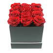 An opulent arrangement of preserved roses is captured in a clean, studio-style photograph that feels both intimate and grand, much like a carefully chosen gift arriving from Canonbury Flowers to a home near Newington Green. The image shows twelve deep crimson roses, their velvety petals fully unfurled, nestled tightly together in a matte black square box. The roses are arranged in a perfectly regular 3x4 formation, each bloom almost touching the next so that the top of the arrangement appears like a plush carpet of red, with only the subtlest variations in height and petal curl adding gentle movement. Every flower is impeccably formed, the rich ruby hue deepening towards the centres, where the light falls more softly and shadows gather among the layers of petals. The box itself has sharp, clean angles and an elegant simplicity, its dark surface broken only by a slim white stripe running horizontally around its lower edge, as if tracing the line of a quiet side street off St. Paul's Road. Against a brilliant white background, with no other objects or colours present, the strong contrast between the black box and the vivid red roses is striking, while delicate shadows along the base and inside the rose clusters provide a sense of three-dimensional depth. The overall mood is contemporary yet timeless, suggesting a romantic gesture that is meant to last-ideal as a long-lasting Valentine's Day surprise, an anniversary keepsake for a couple in Canonbury, or a luxurious accent on a console table in a light-filled N1 apartment.