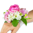 A delicate, wearable bouquet rests on a left wrist and forearm with a light-to-medium skin tone, set against a clean white backdrop that highlights every petal and leaf. At the heart of the corsage sits a large, fully opened deep fuchsia-pink rose whose layered petals spiral outward with plush, velvety texture; a soft, warm rose scent seems almost audible in the quiet studio light. Around the rose, clusters of blush pink hydrangea florets create a cloudlike cushion, their tiny petals adding volume and a subtle, papery texture that contrasts with the rose's dense form. Several pristine white alstroemeria - Peruvian lilies - fan gently from the centre, each bloom showing four to six smooth petals with faint pale-green streaking toward the throat. To the right, a cluster of pale green alstroemeria buds and a few nearly closed pink buds suggest future opening, lending a sense of fresh, unfolding life. Broad, glossy emerald leaves cradle the arrangement, their deep green sheen providing a cool counterpoint to the warm pinks and whites. The corsage is secured with a refined multi-strand bracelet of small lustrous white pearls that encircles the wrist and trails slightly across the back of the hand, giving the piece a timeless, jewellery-like finish. Composed with care and balance, this corsage reads as romantic and sophisticated - an ideal accent for a prom, wedding party, or any formal celebration - evoking the gentle excitement of a first dance or a quiet, blooming memory in Canonbury's springtime streets.