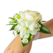 A delicate white wrist corsage rests against fair skin, composed like a small, personal garden worn for a vow or a dance. At its heart sits a creamy ivory rose, petals unfolding with a velvety softness that catches a cool, diffuse light and suggests a quiet, classic romance. Below and slightly to the left, a larger trumpet-shaped white bloom - likely an Alstroemeria (Peruvian lily) - opens toward the viewer, its throat washed with a pale green-yellow that gives the arrangement subtle depth and an almost painterly contrast. Tiny clusters of airy white Gypsophila (Baby's Breath) float between the main flowers, lending a cloud-like softness, while several bright green buds promise further unfurling in the hours after it is worn. Near the wrist a small spray of daisy-like white florets with warm golden centers offers a touch of innocent charm. Broad, glossy deep-green leaves frame and lift the blooms, their waxy texture balancing the petals' fragility. The piece is fastened by a chic multi-strand pearl bracelet - a band of round, lustrous faux pearls that sit cool and smooth against the skin and lend the corsage an heirloom feel. Imagine the subtle, fresh scent of rose and green stems as you move, a gentle reminder of spring mornings. Designed with careful proportion and traditional elegance, this corsage feels quiet and celebratory at once, suited for weddings, proms, and formal evenings where each small gesture bears meaning.