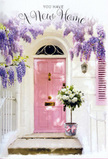 A soft, romantic doorway in Canonbury is framed by a curtain of lavender wisteria that drapes gracefully over a pastel pink front door, creating an atmosphere of calm and gentle anticipation. The door, painted in a warm, powdery blush, stands out against pale, whitewashed walls and a simply painted shutter that together reflect the kind of understated charm found on the quieter streets near Canonbury Station. At the doorstep rests a metal bucket in a muted grey, filled to overflowing with lush white and cream roses, their petals full and velvety, mingling with fresh green foliage that peeks delicately between the blooms. A pale pink ribbon is tied decoratively around the bucket, softening the metal with a hint of satin sheen and tying the bouquet visually back to the rosy hue of the door. Light filters softly through the wisteria above, casting faint, dappled shadows on the stone and lending a tranquil, late-afternoon glow to the entire entrance. There is a sense that these flowers have just been delivered to celebrate moving in: perhaps a thoughtful gift from a friend, marking new keys and new memories in this part of Islington. The scene feels intimate and hopeful, like the first step into a freshly painted home where boxes are still being unpacked. Every element-from the colour palette of blush, white, and green to the tumbling blooms overhead-suggests warmth, welcome, and the quiet joy of beginning again, just the sort of moment a local Canonbury florist loves to create for housewarming deliveries.