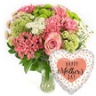 This image portrays a joyful and carefully composed Mother's Day gift pairing: a lush vase arrangement of mixed flowers and a coordinating heart-shaped balloon, both set against a crisp white background that echoes the clean lines of Canonbury's townhouses. The bouquet, positioned to the left, is full and rounded, sitting securely in a clear glass vase that reveals the tidy stems and clear water below. At its centre, soft pink roses unfurl in layered spirals, their petals showing a tender blush that deepens toward the core and fades to gentle, almost ivory-tinged edges. Around them, clusters of coral-pink blossoms, similar to kalanchoe or petite carnations, bring a sense of warmth and texture, while lime green button chrysanthemums introduce a bright, modern twist with their compact, tufted heads. Tiny white, daisy-like chrysanthemums are scattered among the bolder colours, adding a sense of airiness, as if bits of light have settled on the bouquet. Dark green foliage peeks out between the blooms, giving structure and a natural, garden-fresh character. To the lower right, a shiny foil balloon in the shape of a heart completes the scene. The balloon has a white or light silver base patterned with scattered, irregular dots in glimmering gold, silver, and peach, like confetti drifting over the design. In the centre sits a peach-coral heart carrying the inscription HAPPY Mother's DAY in a mix of bold and script black lettering. The overall mood is one of affectionate celebration, as though this set is moments away from being carried through a Canonbury side street and handed to a mum who loves soft colours, fresh flowers, and a little extra sparkle on her special day.