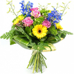 A colourful mixed bouquet is presented upright against a pure white background, its shape and palette carefully composed to create a joyful, contemporary look. At the centre, soft pink roses open in generous spirals, their smooth petals catching the light and suggesting a gentle, romantic mood. These are framed by bright yellow gerbera daisies, whose open faces and deep brown centres resemble miniature suns, radiating warmth and positivity like a stroll through Canonbury's tree-lined streets on a clear day. Punctuating the arrangement with height, tall stems of rich blue delphinium rise elegantly above the rounder blooms, each stem studded with small, individual florets that bring cool contrast and a slightly wild, garden-inspired feel. Surrounding the flowers is an abundance of greenery that gives the bouquet its fullness: delicate fern fronds extend softly beyond the outer edges; clusters of vivid green, textured filler foliage break up the colours and create a sense of lushness; and larger, glossy dark green leaves wrap around the base, forming a sculpted collar that cradles the blooms. Here and there, slim green stems tipped with tiny buds add an airy, unfinished edge, as if the bouquet has just been gathered from a well-tended border in a hidden Canonbury courtyard. The stems are clearly visible at the bottom, drawn together and tied with natural twine, emphasising the hand-tied, freshly made quality. The overall impression is of a bright, uplifting arrangement that would work beautifully as a birthday surprise, a thank-you gesture, or a cheerful centrepiece for a Canonbury flat, bringing colour and the faint, sweet fragrance of roses into the room.